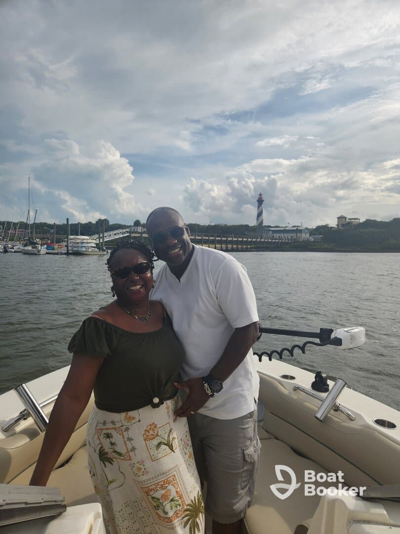 A joyful couple poses together on a boat with a scenic lighthouse in the background, perfect for romantic outings or memorable celebrations on the water.