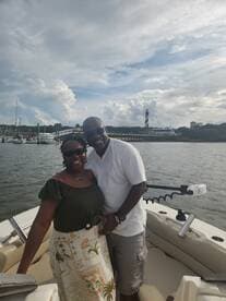 A joyful couple poses together on a boat with a scenic lighthouse in the background, perfect for romantic outings or memorable celebrations on the water.