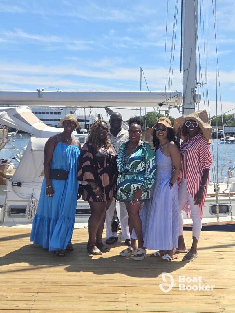 A joyful group of friends poses together on the dock beside a yacht, capturing a moment of celebration and camaraderie before their boating adventure.