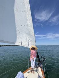 A woman enjoys a sunny day sailing on a boat, showcasing the beauty of the ocean and the joy of being out on the water.