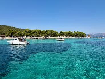 A picturesque view of boats anchored near a beautiful beach with clear turquoise waters, showcasing a perfect summer day on the coast.