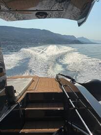 A sleek view from the back of a boat cruising through calm waters, showcasing the stunning reflections and surrounding mountains — perfect for adventure seekers and boating enthusiasts.