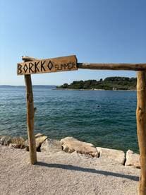 A wooden sign reading 'BORKKO SUMMER' stands by the water's edge, inviting visitors to enjoy the scenic beach and clear waters.