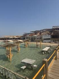 A scenic view of a waterfront area featuring wooden structures and tables in shallow water, ideal for relaxation and dining by the beach.
