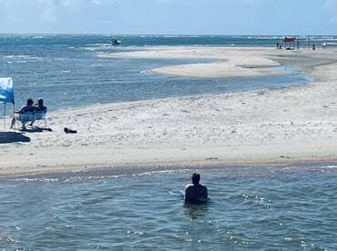 A serene moment at a sandbar with a person enjoying the water while others relax on the beach — perfect for a day of sun and fun.