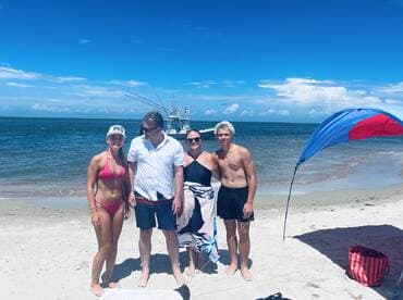 A joyful family poses together on the beach with a boat in the background, capturing a perfect day of sun and fun by the water.