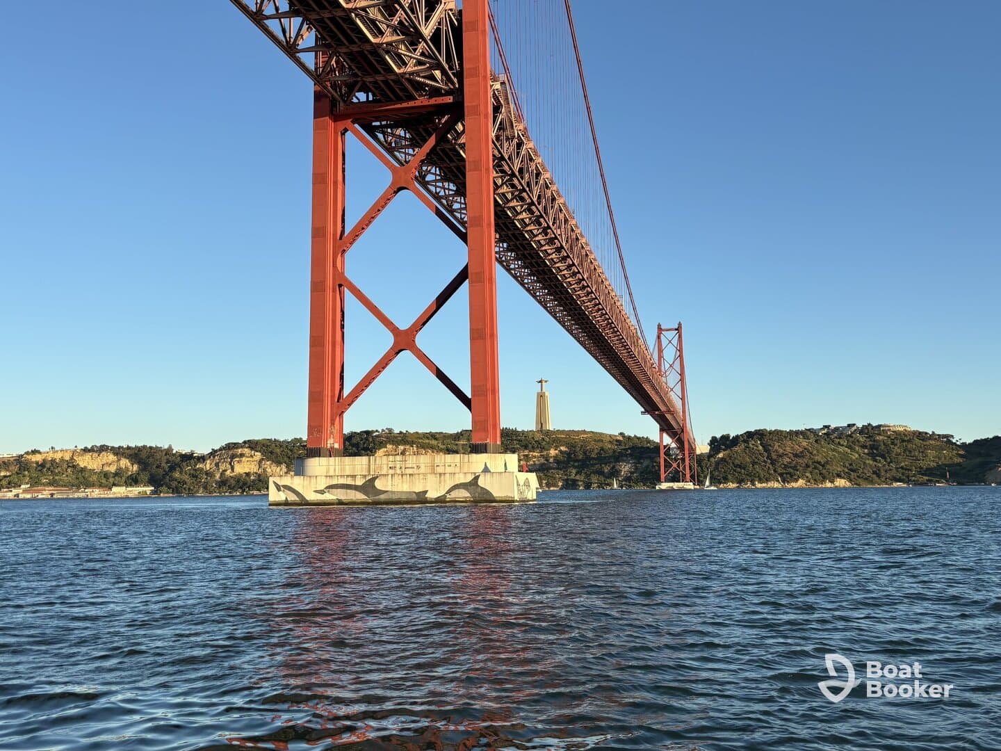 A stunning view of the iconic red bridge spanning over the water, framed by lush hills and clear skies — a perfect representation of the scenic beauty of the area.