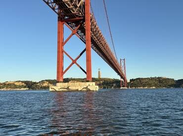 A stunning view of the iconic red bridge spanning over the water, framed by lush hills and clear skies — a perfect representation of the scenic beauty of the area.