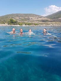 A joyful group swims in the crystal-clear waters near an island, enjoying a refreshing day on the water — perfect for summer adventures.