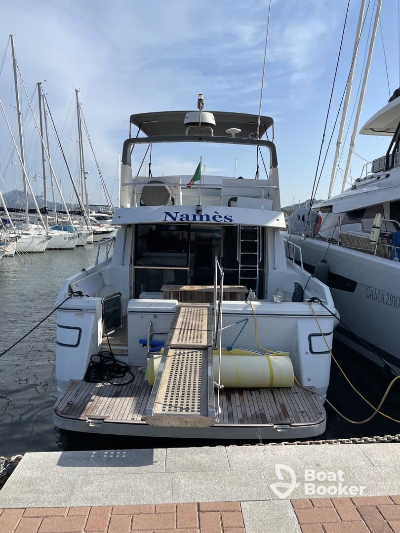 A clear view of the back of a yacht named 'Namès' docked at the marina, showcasing its structure and design against a backdrop of other boats.