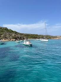 A scenic view of multiple boats anchored in crystal-clear turquoise waters near a beach, showcasing a perfect day for relaxation and water activities.