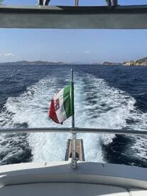 A view from the bow of a boat showcasing the Italian flag as it navigates through clear waters, perfect for scenic cruising or island hopping adventures.