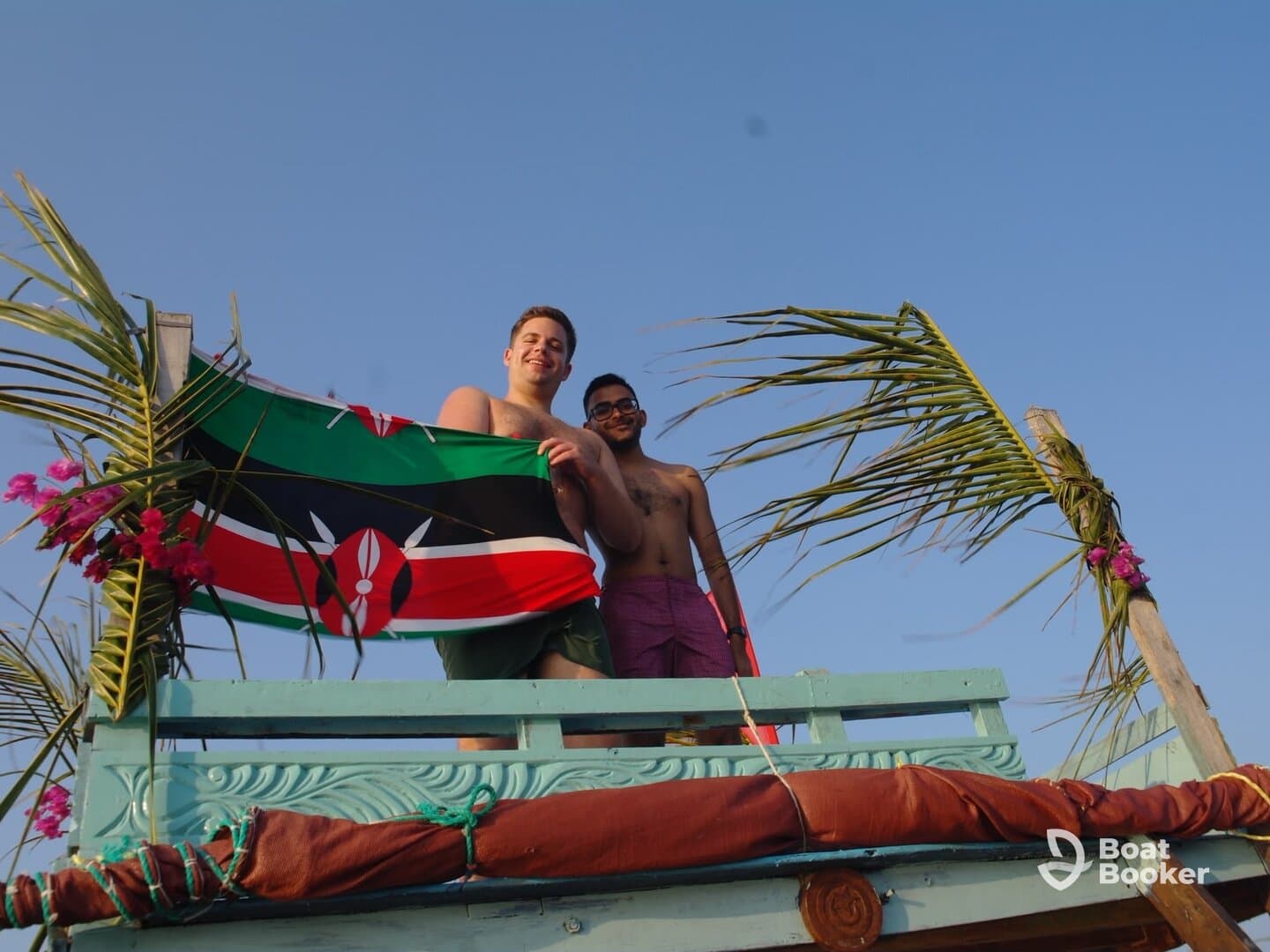 Two friends celebrate on a boat, proudly displaying the Kenyan flag against a clear blue sky — a perfect moment of camaraderie and adventure on the water.