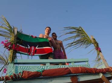 Two friends celebrate on a boat, proudly displaying the Kenyan flag against a clear blue sky — a perfect moment of camaraderie and adventure on the water.
