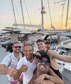 A joyful group of friends poses for a selfie at a marina during sunset, capturing the essence of camaraderie and celebration on the water.