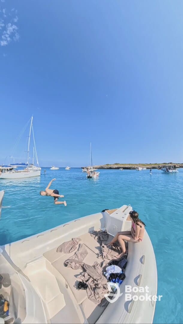 A lively scene captures a child jumping into the crystal-clear waters while a girl relaxes on the boat, showcasing the fun and excitement of a day on the water.