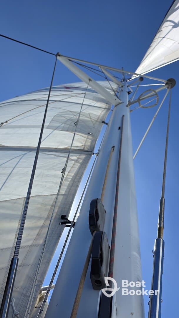 A close-up view of the mast and sails of a sailboat against a clear blue sky, showcasing the intricate rigging and sail design.