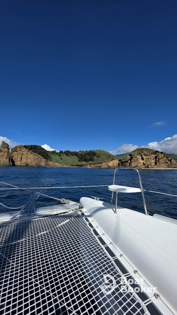 A serene view from the deck of a catamaran, showcasing stunning coastal cliffs and clear blue skies — perfect for exploring picturesque destinations.