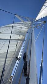 A close-up view of the mast and sails of a sailboat against a clear blue sky, showcasing the intricate rigging and sail design.
