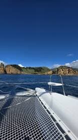 A serene view from the deck of a catamaran, showcasing stunning coastal cliffs and clear blue skies — perfect for exploring picturesque destinations.