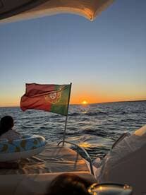 A serene sunset view from a boat, featuring a Portuguese flag and a child enjoying the moment — a perfect scene for family outings on the water.