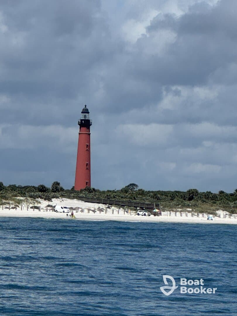 A picturesque view of a red lighthouse standing tall against a backdrop of cloudy skies and a sandy coastline, perfect for capturing the beauty of coastal landscapes.