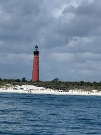 A picturesque view of a red lighthouse standing tall against a backdrop of cloudy skies and a sandy coastline, perfect for capturing the beauty of coastal landscapes.