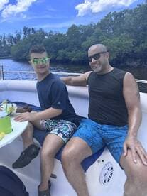A joyful moment on the water as a young man and an adult enjoy their time together on a boat, surrounded by lush greenery — perfect for family outings and bonding experiences.
