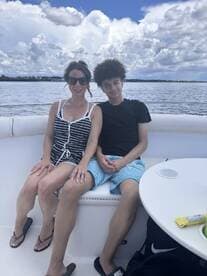 A mother and her son enjoy a relaxing moment together on a boat, surrounded by beautiful water and clouds — perfect for family outings on the water.