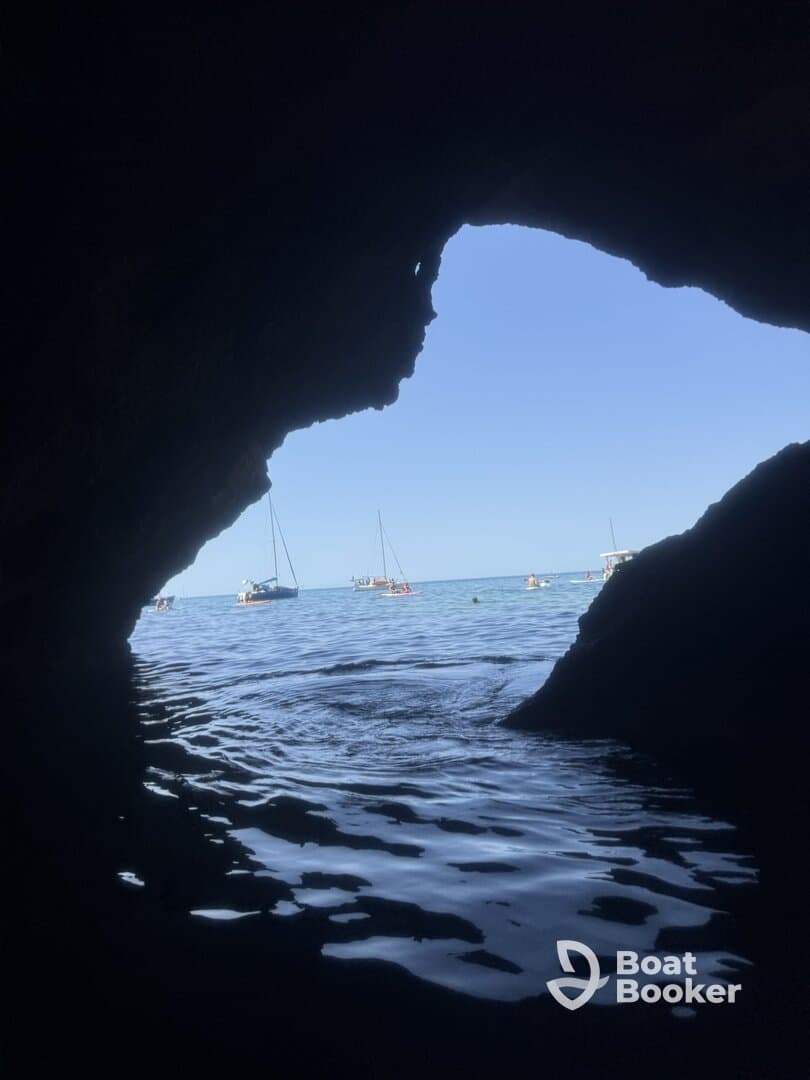 A stunning view from inside a cave, framing boats anchored in a serene harbor — a perfect spot for exploring coastal beauty.