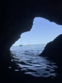 A stunning view from inside a cave, framing boats anchored in a serene harbor — a perfect spot for exploring coastal beauty.