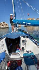 A man adjusts the sail on a sailboat while enjoying a calm day on the water, showcasing the beauty of sailing and the surrounding scenery.