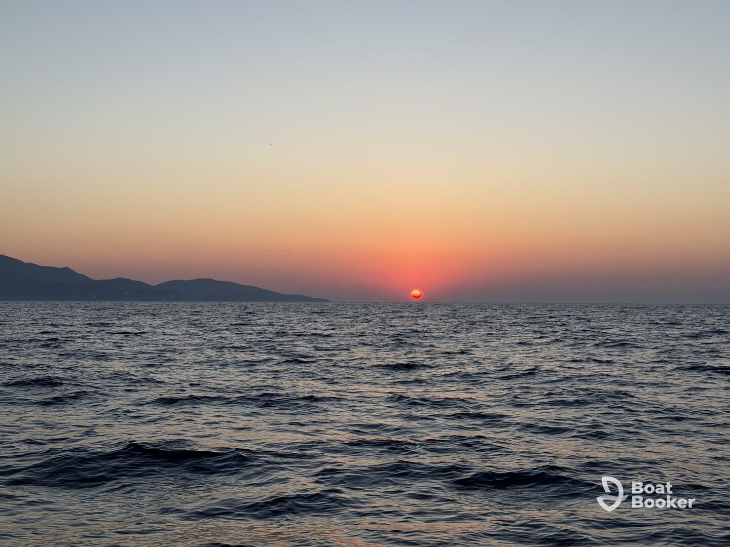 A stunning sunset over the ocean, with gentle waves and distant mountains creating a serene backdrop — perfect for capturing the beauty of nature at sea.