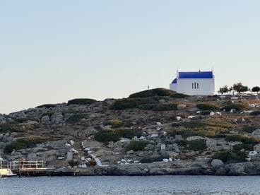 A picturesque view of a white chapel with a blue dome on a rocky island, showcasing the serene beauty of the landscape — perfect for capturing memorable moments during a boat trip.