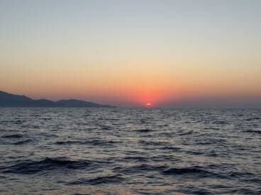 A stunning sunset over the ocean, with gentle waves and distant mountains creating a serene backdrop — perfect for capturing the beauty of nature at sea.