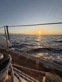 A serene sunset view from the deck of a sailboat, showcasing the tranquil waters and distant mountains — perfect for sunset cruises.