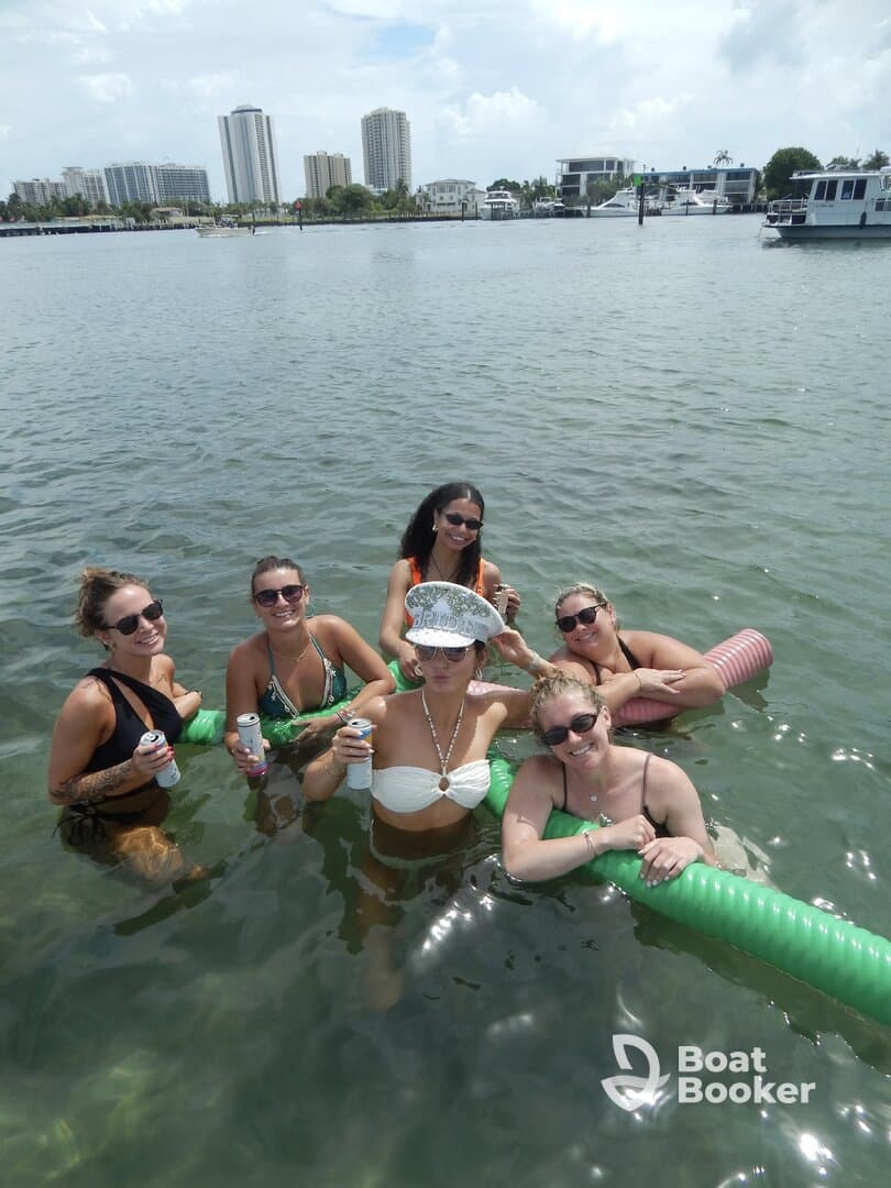 A fun group of friends enjoys a lively day in the water, celebrating with drinks and floating on pool noodles — perfect for a summer party on the water.