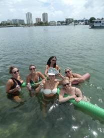 A fun group of friends enjoys a lively day in the water, celebrating with drinks and floating on pool noodles — perfect for a summer party on the water.