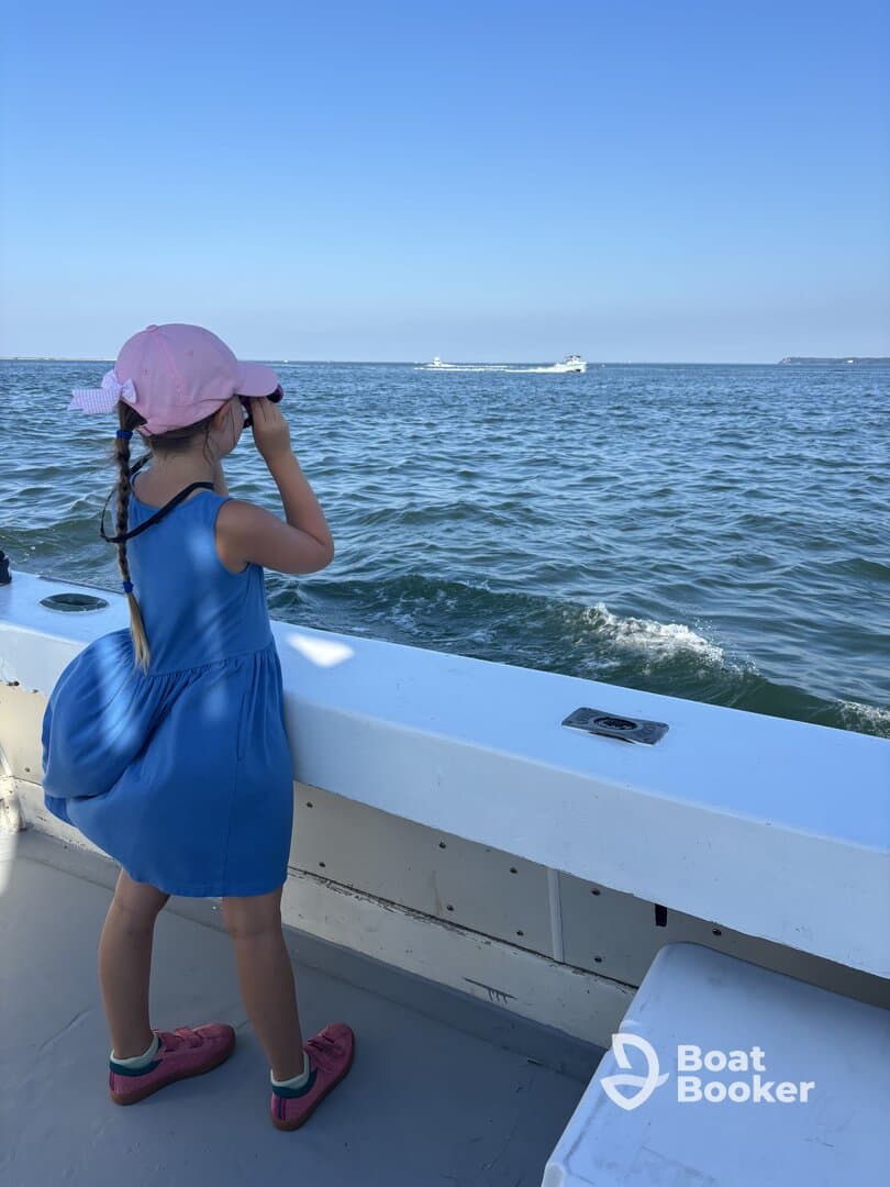 A young girl uses binoculars to explore the ocean from the deck of a boat, capturing the spirit of adventure and discovery on the water.