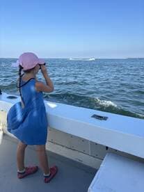 A young girl uses binoculars to explore the ocean from the deck of a boat, capturing the spirit of adventure and discovery on the water.