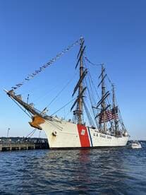 A majestic view of the U.S. Coast Guard tall ship, adorned with colorful flags, docked and ready for visitors — a perfect representation of maritime heritage.