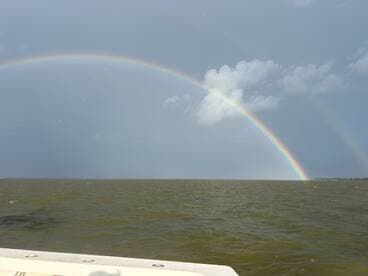 A stunning view of a double rainbow arching over the water, set against a dramatic stormy sky — a perfect backdrop for memorable boating adventures.
