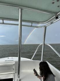 A scenic view from a boat featuring a vibrant rainbow in the sky, with a guest enjoying the moment while holding a phone — a perfect snapshot of a memorable boating experience.