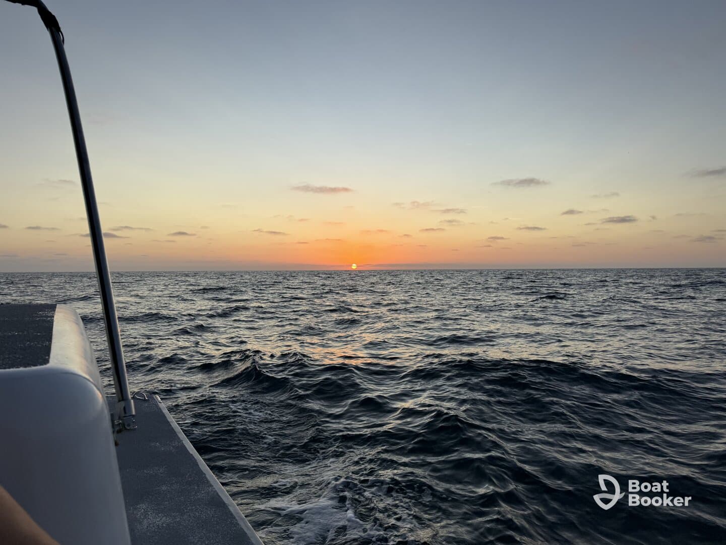A serene sunset view from the side of a boat, showcasing the tranquil ocean waves and the vibrant colors of the sky as the sun sets on the horizon.