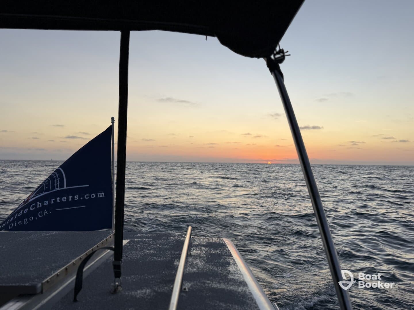 A serene sunset view from the deck of a boat, showcasing the tranquil waters and the boat's flag — perfect for sunset cruises in San Diego.