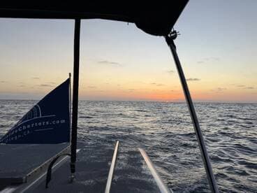 A serene sunset view from the deck of a boat, showcasing the tranquil waters and the boat's flag — perfect for sunset cruises in San Diego.
