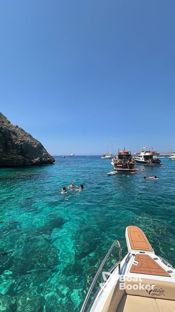 A lively scene of people swimming in crystal-clear waters, with several boats anchored nearby, perfect for a fun day out on the water.