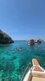 A lively scene of people swimming in crystal-clear waters, with several boats anchored nearby, perfect for a fun day out on the water.