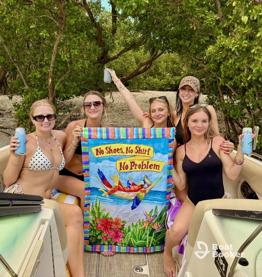 A lively group of friends celebrates with drinks and a fun banner on a boat, embodying the carefree spirit of a beach day — perfect for summer adventures.