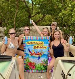 A lively group of friends celebrates with drinks and a fun banner on a boat, embodying the carefree spirit of a beach day — perfect for summer adventures.
